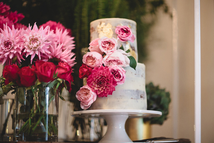 Semi naked wedding cake with gold foil and tiopped with vibrant flowers